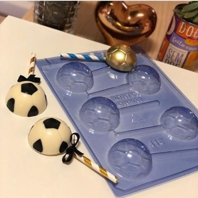 Forma de silicone azul e bolas decorativas brancas e pretas com paus e laços num fundo branco