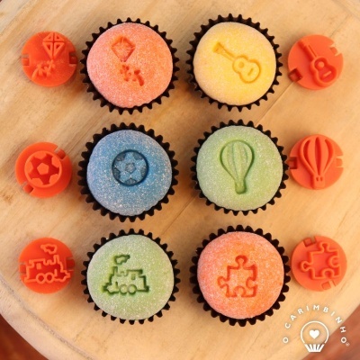 cupcakes coloridos com desenhos em relevo e moldes laranja numa placa de madeira