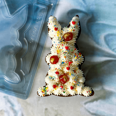 Bolo em forma de coelho com chantili e decoração colorida ao lado de embalagem plástica