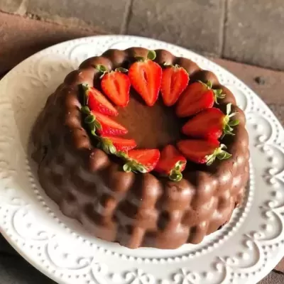 Bolo de chocolate com morangos cortados ao meio no topo, em prato branco decorado.