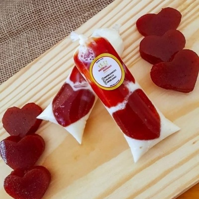 Duas embalagens de gelado bicolor e gelados em forma de coração sobre bandeja de madeira clara.