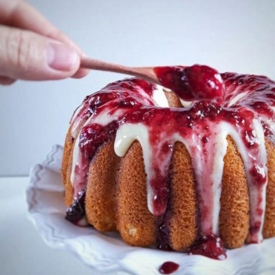 Bolo com cobertura branca e calda vermelha servido num prato branco