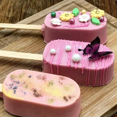 Três gelados cor-de-rosa em pau de madeira com decoração variada sobre tabuleiro de madeira