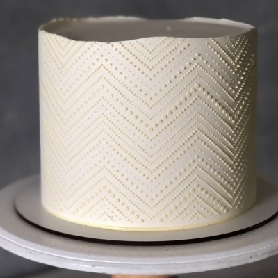 Bolo branco redondo com padrão de pontos dourados em ziguezague