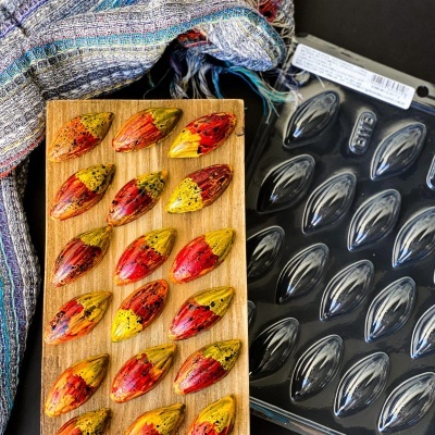 Forma plástica para chocolates com chocolates vermelhos e amarelos em base de madeira e tecido ao fundo