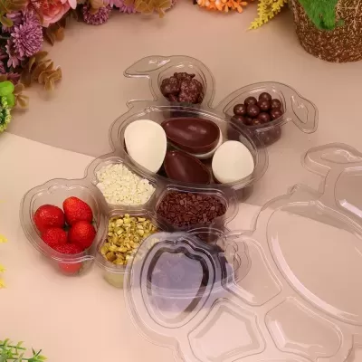 Embalagem transparente em forma de tartaruga com doces variados sobre superfície bege e flores