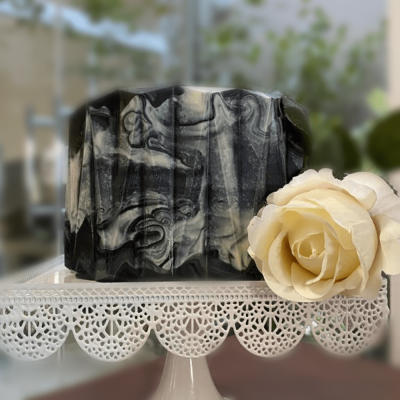 Barra de sabão marmoreada cinzento e preto ao lado de uma flor branca num suporte decorativo branco