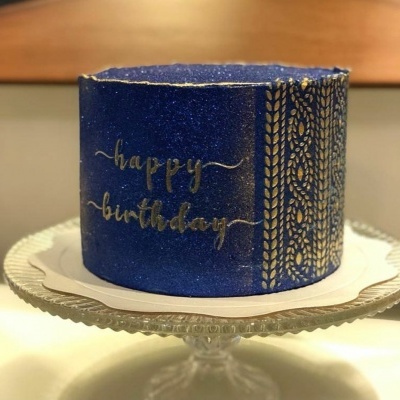 Bolo azul glitter com escrita dourada Happy birthday numa base de vidro