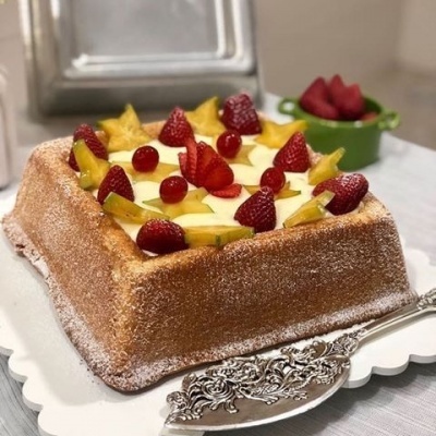 Bolo quadrado com creme e frutas frescas numa travessa branca com espátula prateada