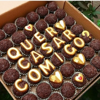 Brigadeiros e chocolates em forma de letras douradas com frase romântica numa caixa de cartão