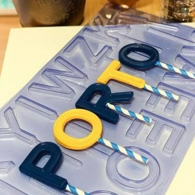 Forma de silicone translúcido com letras coloridas formando a palavra PORTO com espetos listrados azuis e brancos