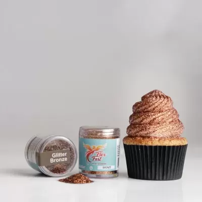 Cupcake com cobertura brilhante bronze ao lado de dois frascos de glitter bronze, um com rótulo 'Glitter Bronze' e 'Eden Fest'.