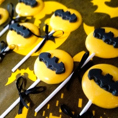 Pirulitos amarelos decorados com morcegos pretos e fitas negras, em fundo temático de Halloween.