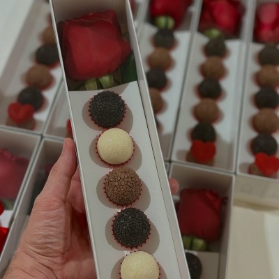 Caixa branca com uma rosa vermelha e cinco brigadeiros coloridos dentro.