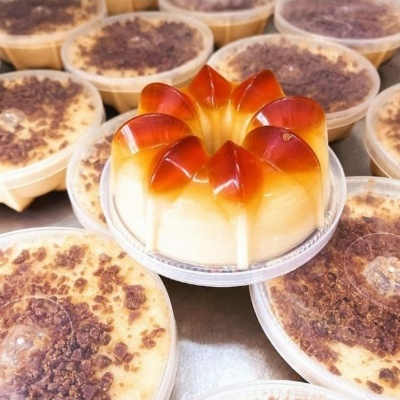 Pudins em embalagens plásticas, um com gelatina laranja em forma de flor, outros com cobertura de chocolate.