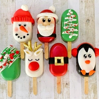 Oito gelados decorativos de Natal variados em pauzinhos, incluindo boneco de neve, Papai Noel, árvore de Natal, rena, cinto de Papai Noel e pinguim.