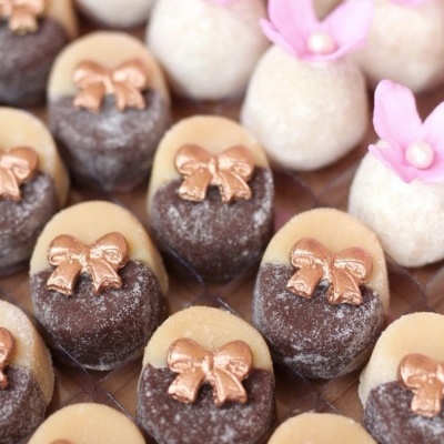 Doces decorados com laços dourados e flores rosas sobre base de madeira