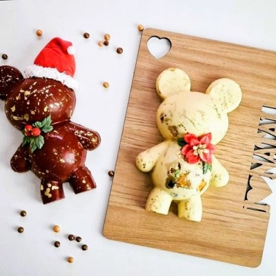 Dois brinquedos ursinho decorativos, castanho com gorro vermelho e amarelo claro sobre tábua de madeira