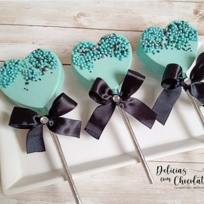 Pirulitos de coração azuis com laço preto e decoração em prato branco