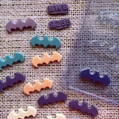 Botões coloridos em forma de morcego e retângulo com texto sobre tecido bege