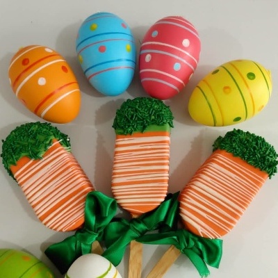 Ovos decorativos coloridos e palitos de cenoura decorativos com fitas verdes num fundo branco