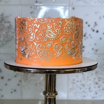 Bolo laranja com decoração prateada em relevo sobre suporte metálico.