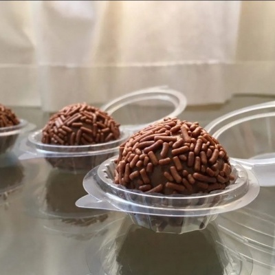 Três brigadeiros de chocolate com granulados em embalagens plásticas transparentes.