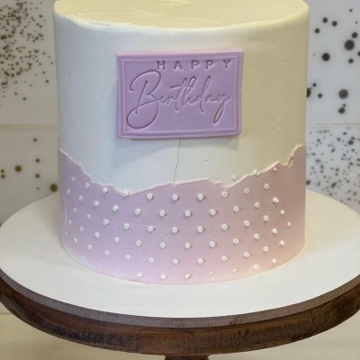 Bolo redondo branco e rosa com pontos brancos e placa HAPPY Birthday
