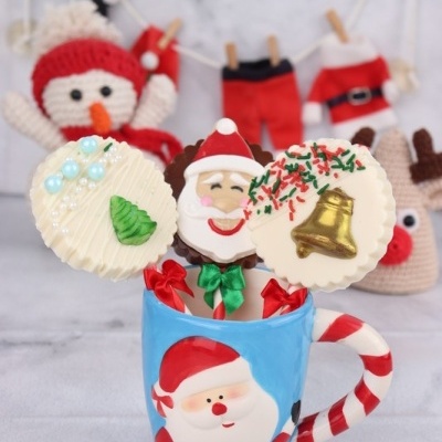 Caneca de Papai Noel com palhetas de chocolate decoradas e bonecos natalinos crochê ao fundo