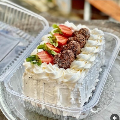 bolo decorado com morangos, brigadeiros e creme branco numa caixa plástica