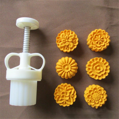 Molde branco com seis bolos amarelos em padrão floral numa superfície castanha