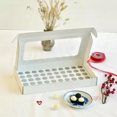 Caixa branca de cartão com tampa transparente e orifícios circulares para bombons