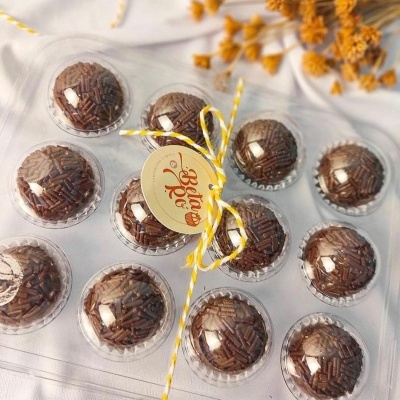 Pacote transparente com 12 brigadeiros cobertos por granulados de chocolate e etiqueta amarela