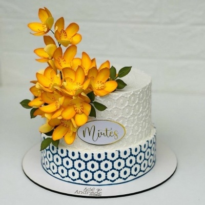 bolo decorativo branco e azul com flores amarelas e placa com nome