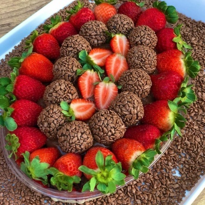 Tigela transparente com brigadeiros e morangos frescos sobre bandeja branca