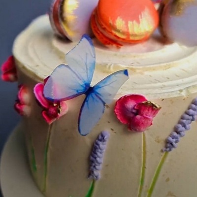 Bolo decorado com flores, macarons e borboleta azul