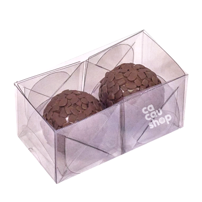 Dois brigadeiros decorados em caixa transparente com logotipo 'cacau shop'