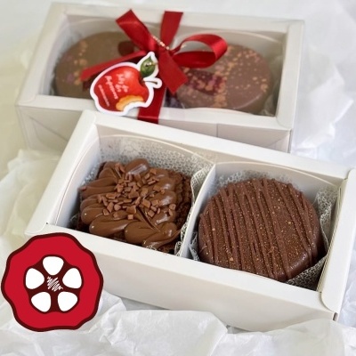 Caixas brancas com doces de chocolate, uma com tampa transparente e laço vermelho, outra aberta com dois doces dentro