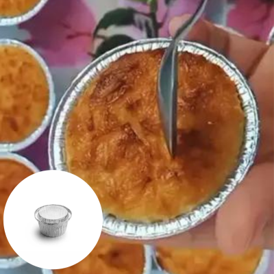 Doce dourado em recipiente de alumínio com colher a cortar a superfície, fundo com mais doces e tecido floral.