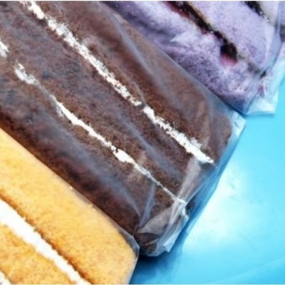 Três bolos fatiados de cores diferentes embalados em plástico sobre fundo azul