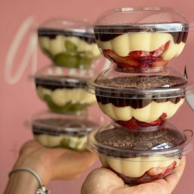 Copos plásticos transparentes empilhados com camadas de creme amarelo e frutas, fundo rosa