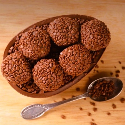 Taça de chocolate oca recheada com brigadeiros cobertos de granulados de chocolate e colher com granulados