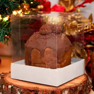 Bolo de chocolate com cobertura dentro de caixa transparente sobre superfície de madeira com decoração natalícia