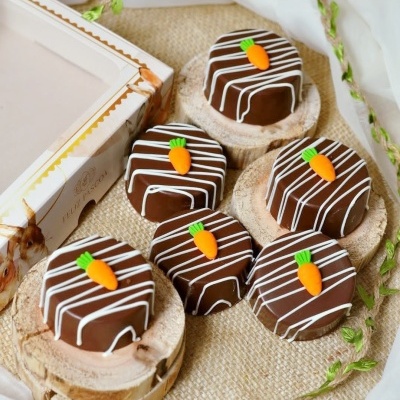 Doces de chocolate com decoração branca e enfeites de cenoura sobre bases de madeira.