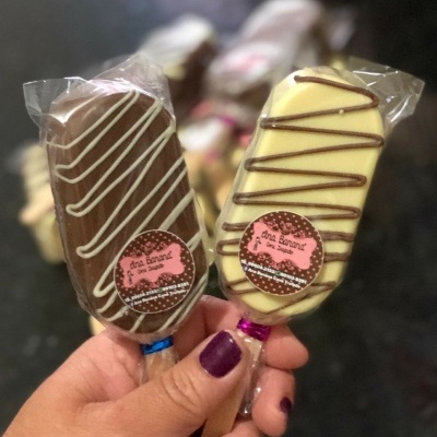 Dois gelados em palito cobertos por chocolate e decorados, embalados em plástico transparente com etiqueta rosa
