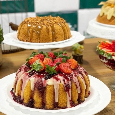 Dois bolos bundt decorados, um com morangos e glacê branco e vermelho e outro com cobertura castanha granulada em pratos brancos