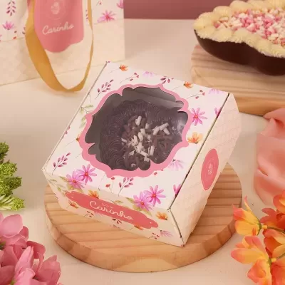 Caixa decorativa branca com flores, mostrando brigadeiro com coco ralado em base de madeira