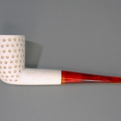 Cachimbo esbranquiçado com padrão de buracos e cabo âmbar translúcido sobre fundo cinzento