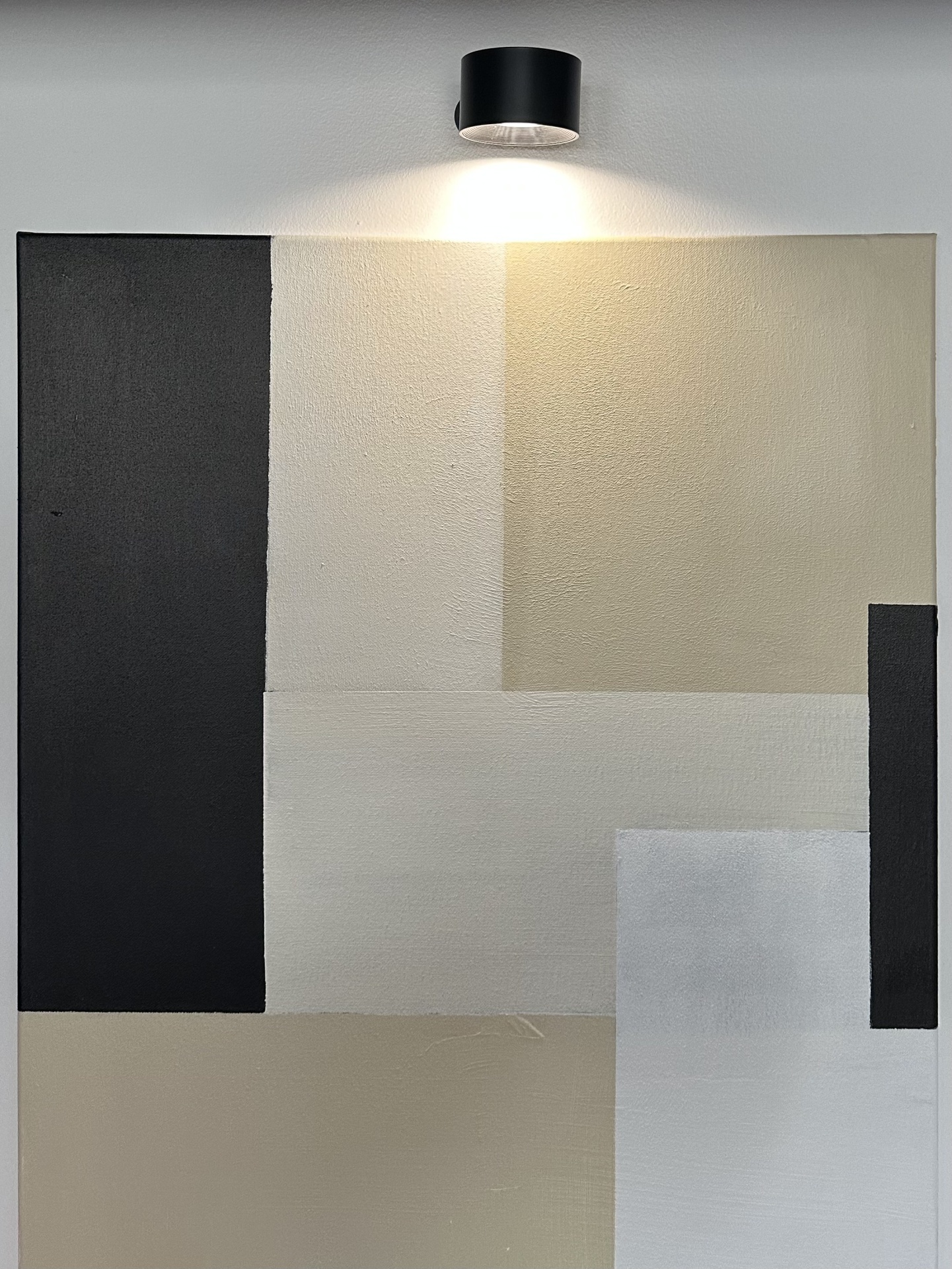 quadro abstrato com retângulos em preto, branco, cinza e bege, iluminado por luz superior
