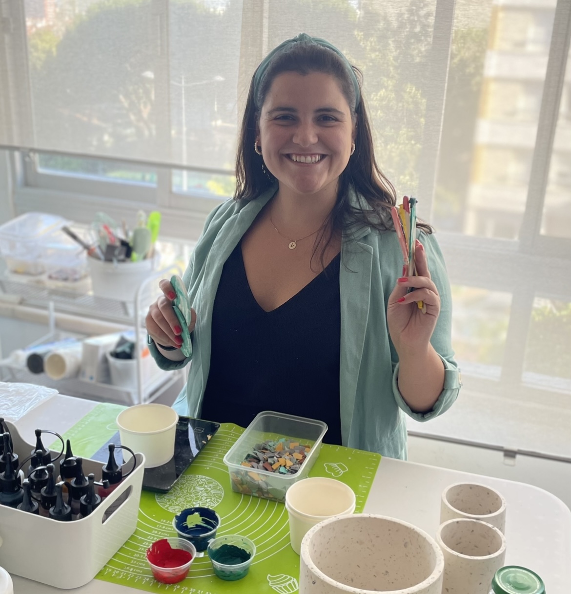 Pessoa com pincéis coloridos sentada numa mesa com tintas e recipientes diversos